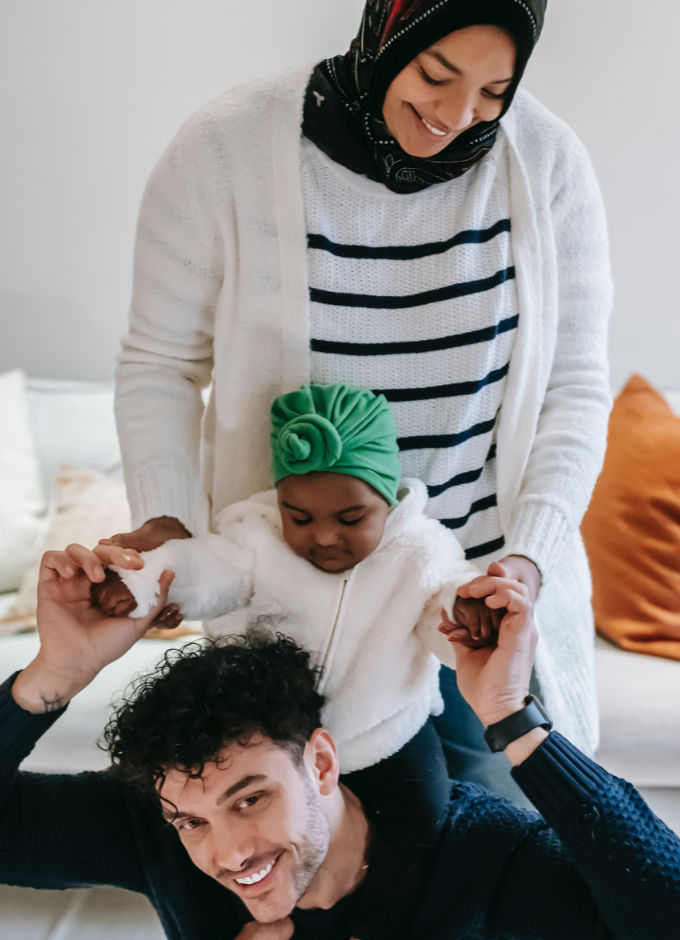 A young multiracial family. Child is sitting on father's shoulder and mother is holding the child