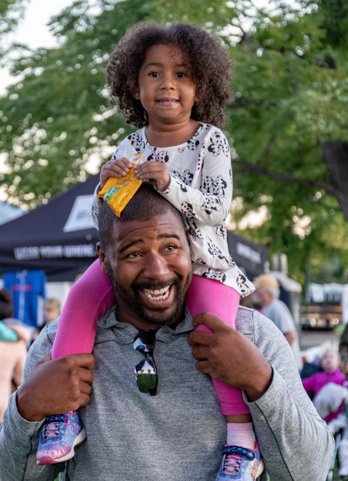 An African Canadian father with his daughter on top of his shoulder